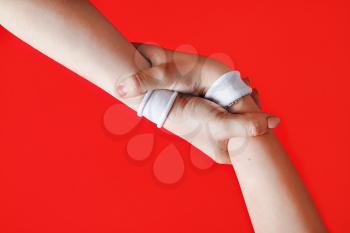 Helping hands concept. Hands with white bracelets on red backgroung.