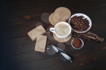 Still life with coffee cup, coffee beans, ground powder, beer coasters, blank kraft business cards and glasses on wooden background. Top view. Flat lay.