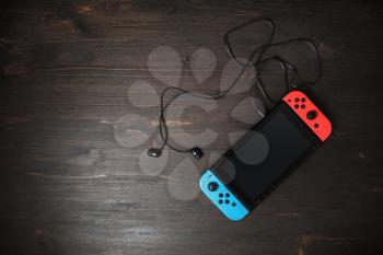 Minsk, Belarus - May 07, 2020: Nintendo Switch game console with blank black screen and headphones on wooden background. Copy space for text. Flat lay.