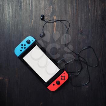 Minsk, Belarus - May 07, 2020: Nintendo Switch game console with white screen and bright joy-con controllers and headphones on vintage wood table background. Flat lay.
