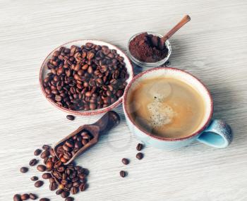 Fresh tasty coffee. Coffee cup, coffee beans and ground powder on light wooden background.
