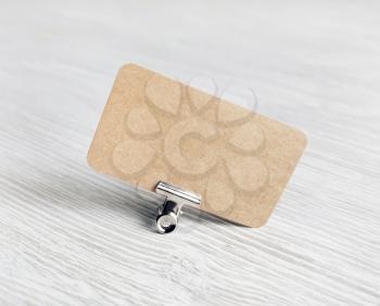Photo of blank brown paper business card and binder clip on light wood table background. Mockup for branding identity.