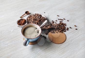Delicious fresh coffee. Coffee cup, coffee beans, ground powder and beer coaster on light wood table background.