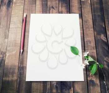 Blank white letterhead, pencil, eraser and cherry flowers on vintage wooden table background. Responsive design mockup.