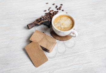 Blank kraft paper business cards, coffee cup and roasted coffee beans on light wooden background.