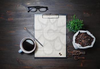 Clipboard with blank kraft paper, coffee cup, plant, coffee beans in canvas bag, glasses and pencil on wood table background. Flat lay.