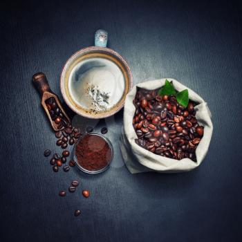 Cup of coffee, roasted coffee beans in a sack and ground powder on black table background. Top view. Flat lay.