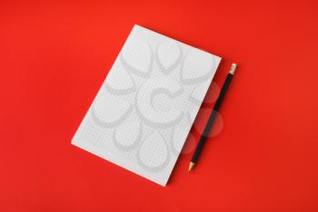 Blank stationery mockup. Blank copybook and pencil on red paper background. Template for placing your design.