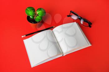 Blank book, glasses, plant and pencil on red paper background. Stationery elements. Template for placing your design.