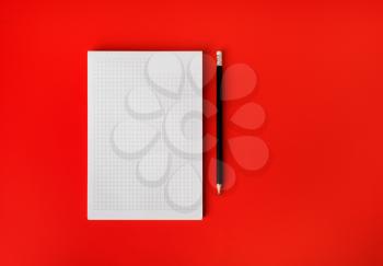 Blank copybook page and pencil on red paper background. Space for text. Mockup. Top view. Flat lay.