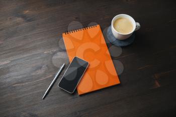 Smartphone, blank notepad, coffee cup and pen on wooden background. Template for placing your design.