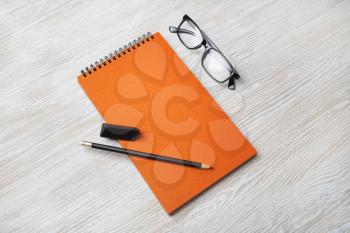 Orange notebook, glasses, pencil and eraser on light wood table background. Branding mock up.