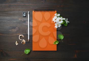Orange notepad, pencil, sharpener and flowers on wooden background. Blank stationery set. Top view. Flat lay.