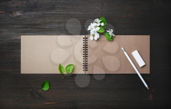 Photo of blank kraft sketchbook, pencil, eraser and spring flowers on wooden background. Template for placing your design. Flat lay.