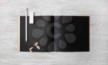 Blank black booklet, pencil and eraser on light wooden background. Branding mock up. Flat lay.