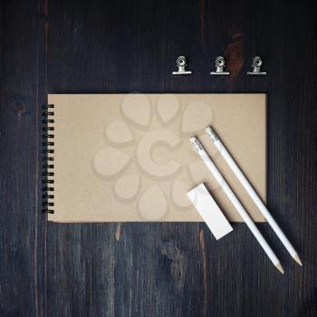 Photo of closed blank kraft sketchbook, pencils and eraser on wood table background. Template for placing your design. Flat lay.