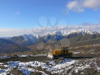 Crawler tractor with grederom against the backdrop of snow-capped mountains. Alignment grederom area for technological needs.