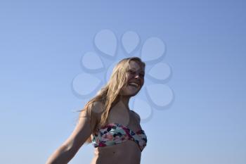 Blonde girl with her hair on blue sky background. Beautiful young woman in a colorful bikini.