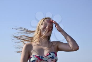 Blonde girl with her hair on blue sky background. Beautiful young woman in a colorful bikini.