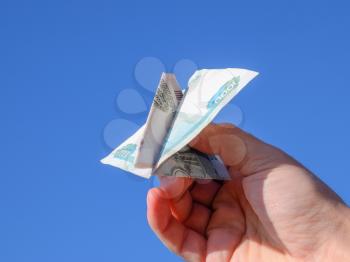 Denominations of Russian money, folded in the airplane against the blue sky in hand.