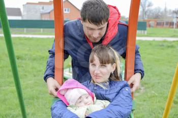Young married couple with child in playground. Young family on a swing.