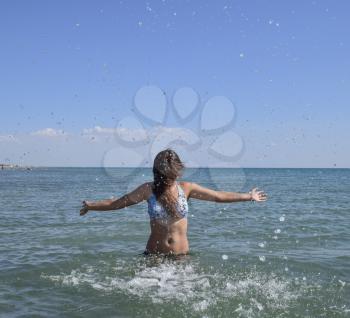 She sprinkles in seawater. Flying up spray from the water throws. The girl with dark hair and a bathing enjoys sea.