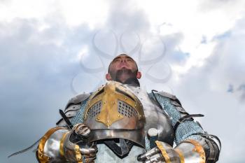 Knight in armor on the background of a cloudy sky. Knightly armor and weapon. Semi - antique photo.
