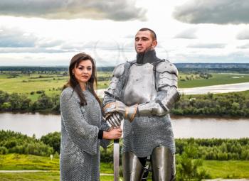 Knight with his lady in armor and chain mail. Knightly armor and weapon. Semi - antique photo.