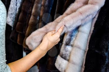 The girl touches the fur on the fur coat. Choosing a fur coat in the store.