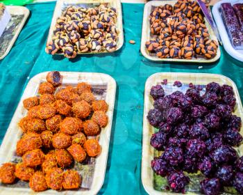 Marmalade balls, sprinkled with dried berries and sweet sawdust. Balls with nuts and marmalade. Trays with Indian sweets. Kozinaki and marmalade.