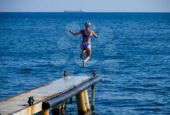 A beautiful girl in a blue bikini jumps from the pier into the water. Jumping in the sea.