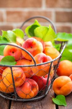Fresh apricots with leaves in basket on wooden table