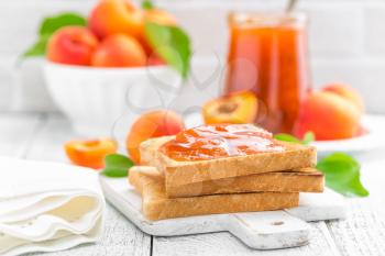 Toasts of bread with apricot jam and fresh fruit with leaves on white wooden table. Tasty breakfast.