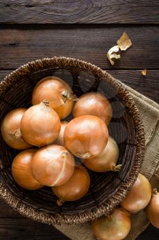 Fresh onion in basket on wooden table, top view