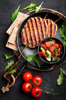 Juicy grilled chicken meat lula kebab on skewers with fresh vegetable salad on black background, top view