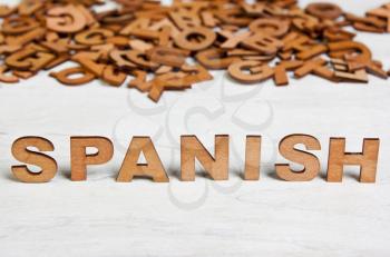Word Spanish made with wooden letters on a background of other blurred letters