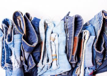 Many different blue jeans in a row on a white background