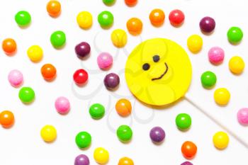 Lollipops, candy smile on, are scattered around the colorful jelly beans on a white background.. Top view, flat
