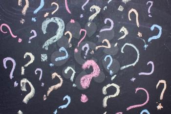 Multicolored question marks are painted with chalk on a blackboard.uncertainty or doubt concept