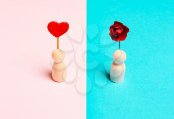 Female wooden figure with heart and male with flower on blue pink background. Concept of love, romance