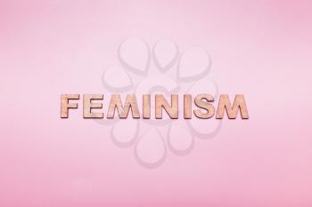 The word feminism in wooden letters on a pink background