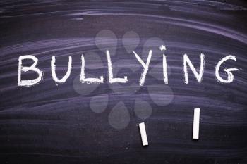 word bullying is written on the blackboard with chalk.
