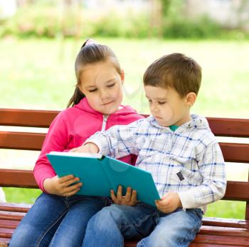 Little boy and girl is reading book while sitting on green grass outdoors