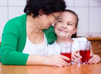 Grandmother with her grandchildren drink fruit juice, indoors