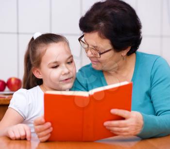 Grandmother is reading book with her granddaughter, indoors
