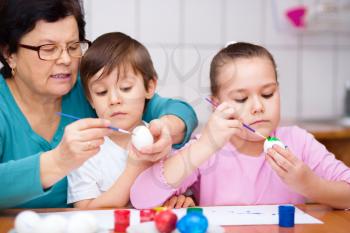 Grandmother with her grandchildren are coloring eggs for Easter, indoors