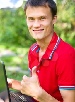 Young man is playing on laptop and showing thumb up sign, outdoor shoot