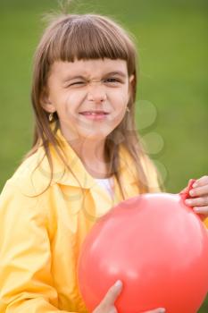 Little girl is inflating red balloon outdoors
