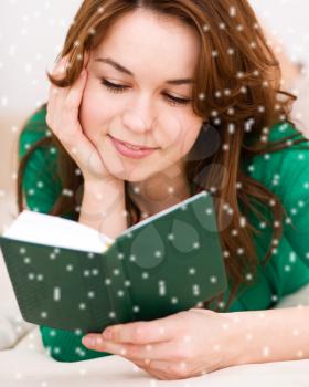 Young woman is reading book while sitting on a couch, over snowy background