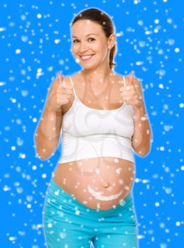 Image of pregnant woman touching her belly with hands, over blue snowy background